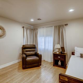 A cozy bedroom featuring a recliner chair, bed, nightstand with a lamp, and soft curtains.
