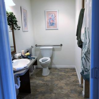 A small, neatly organized bathroom with a toilet, sink, mirror, and wall art.