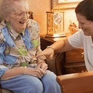 An elderly woman sharing a joyful moment with her caregiver in a cozy home setting.