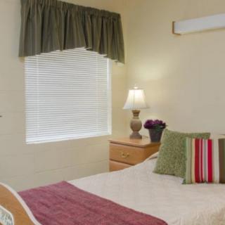 A cozy bedroom with a neatly made bed, bedside lamp, and a window with blinds and curtains.