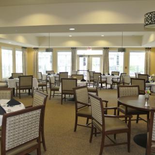 An elegantly arranged dining room with multiple tables and chairs, featuring large windows that allow natural light to flood in.