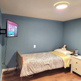 A neatly arranged bedroom with a wall-mounted TV, single bed, and nightstand.