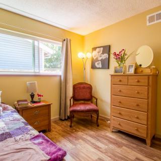 A cozy bedroom with wooden flooring, featuring a dresser and a chair near the window.