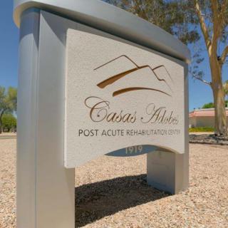 A sign for Casas Adobes Post Acute Rehabilitation Center set against a sunny outdoor backdrop.