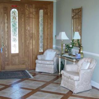 A well-appointed foyer featuring a wooden door, two armchairs, a decorative mirror, and a side table with lamps.