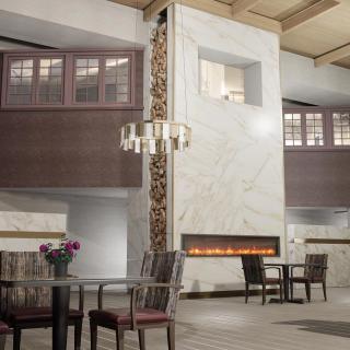 A modern hotel lobby featuring a marble fireplace, elegant chandelier, and comfortable seating.