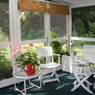 A cozy sunroom with white furniture and lush greenery.