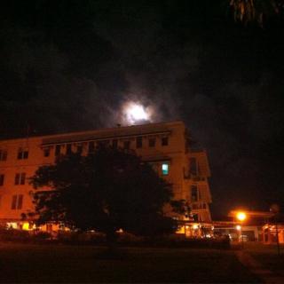 A nighttime view of a building with the moon shining above and trees silhouetted in the foreground.