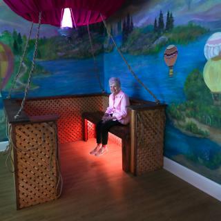 A woman seated in a creatively decorated room with a mural of hot air balloons and colorful lighting.