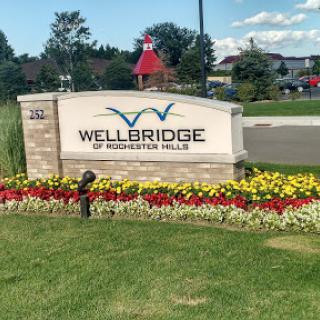 The entrance sign of Wellbridge at Providence Park, surrounded by vibrant flowers.
