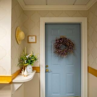 A cozy hallway featuring a blue door adorned with a wreath and a shelf with flowers.