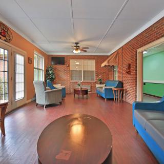 A cozy living room with brick walls, featuring several chairs and a coffee table, illuminated by natural light through large windows.
