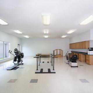 A spacious and well-lit fitness room equipped with exercise machines and a rehabilitation area.
