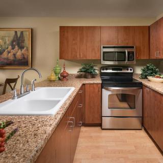 A modern kitchen with wooden cabinets and granite countertops, featuring a double sink, oven, and microwave.