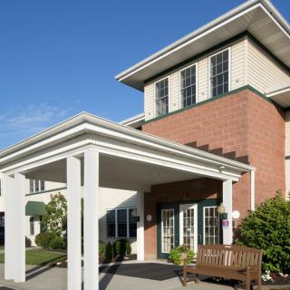 A building with a brick exterior and a covered entrance, featuring a bench and surrounding landscaping.