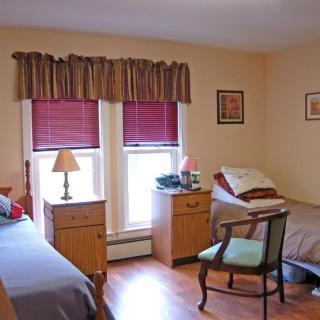 A cozy bedroom with two single beds, nightstands, and a chair by the windows.