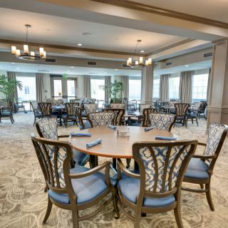 A spacious dining room with elegantly set tables and stylish chairs, featuring large windows and chandeliers.