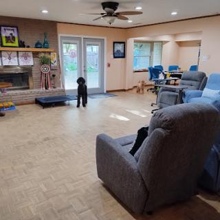 A spacious living room featuring comfortable blue chairs, a cozy fireplace, and a friendly dog.