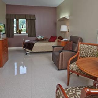 A well-furnished hospital room with a bed, chairs, and a small table.