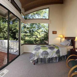 A cozy bedroom with large windows overlooking trees, allowing natural light to fill the modern interior.