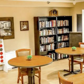A cozy library space with bookshelves, tables, and chairs for reading.