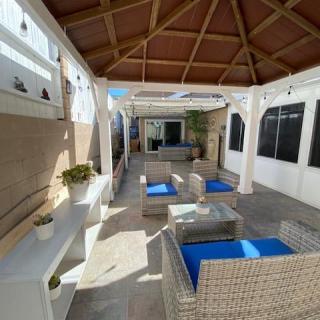 A modern outdoor patio with wicker furniture and a wooden pergola, bathed in sunlight.