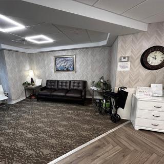A cozy and stylish living room featuring a black sofa, decorative artwork, and a classic wall clock.