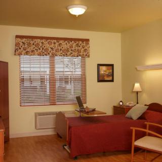 A cozy bedroom with a neatly made bed, wooden furniture, and a window with blinds.