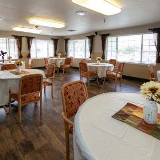 A cozy dining room with round tables, decorated with flowers, and natural light streaming through large windows.