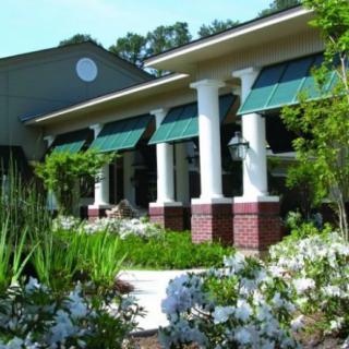 A scenic view of a building with columns and green awnings, surrounded by lush garden landscaping.