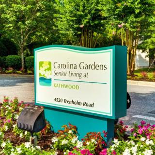 Outdoor sign for Carolina Gardens Senior Living surrounded by trees and flowers.
