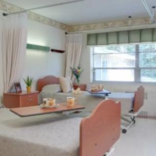 A clean and neatly arranged hospital room with two beds, a window, and curtains.