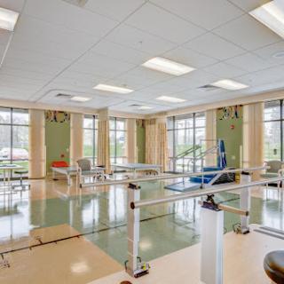 A spacious rehabilitation room equipped with therapy bars and exercise equipment, featuring ample natural light.