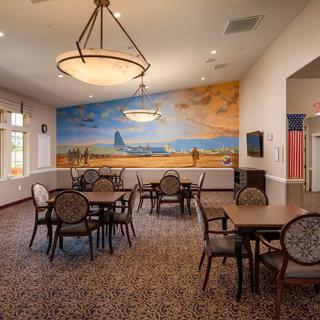 A cozy dining room with tables and chairs, featuring a large mural on the wall and warm lighting.