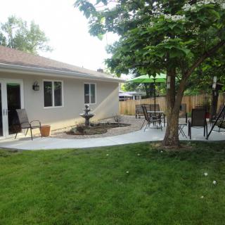 A backyard with a patio featuring outdoor furniture, a fountain, and a well-maintained lawn surrounded by trees.