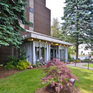 The entrance of a building surrounded by well-maintained landscaping, featuring trees and shrubbery.
