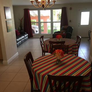 A cozy dining area with tables covered in colorful striped tablecloths, adjacent to a living room with large windows.