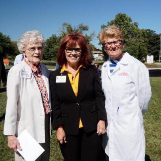 Three women standing together outdoors, two in professional attire and one in a lab coat.