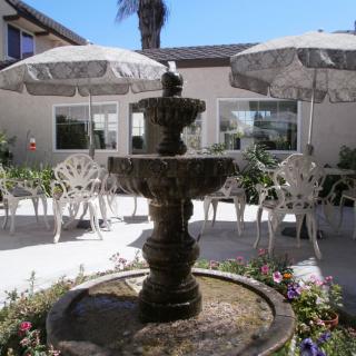 A peaceful outdoor patio featuring a central fountain surrounded by chairs, tables, and umbrellas.