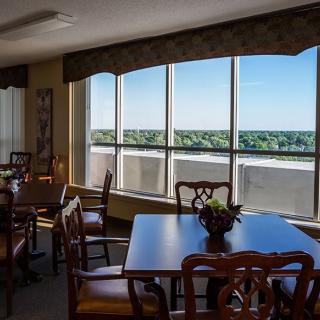 A dining area with wooden tables and chairs, featuring a large window offering a scenic view.