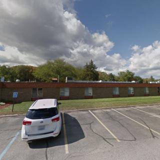 A parking lot with a single car parked in front of a brick building on a cloudy day.