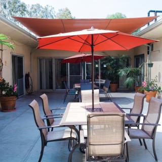 A cozy patio with a table, chairs, and a red umbrella, surrounded by plants in a courtyard setting.