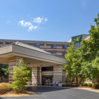 A modern hotel entrance with surrounding trees and a clear blue sky.
