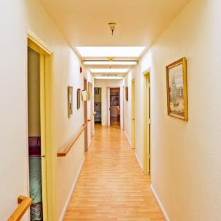 A well-lit hallway with a wooden floor, lined with doors and decorated with paintings.