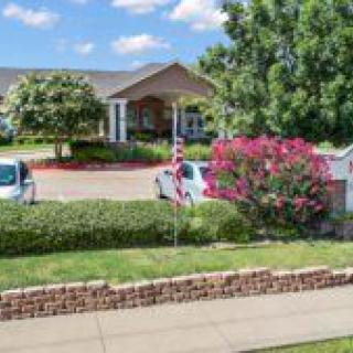 A landscaped entrance to a building with trees and cars parked in the driveway.