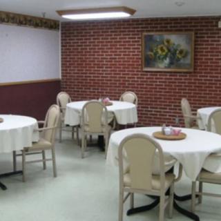 A cozy dining area with tables and chairs arranged neatly, adorned with tablecloths and a flower painting on the brick wall.