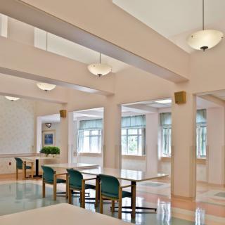 A quiet library space with tables and chairs, illuminated by natural light through large windows.
