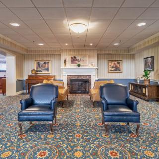 A traditional living room with blue chairs, a patterned carpet, and a fireplace.