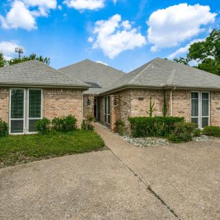 A brick residential house with a driveway under a partly cloudy sky.