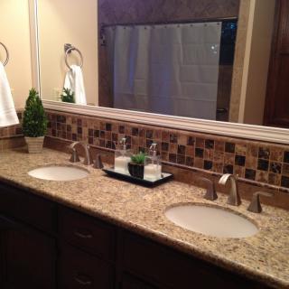 A modern bathroom with a double sink vanity featuring a granite countertop and decorative plants.